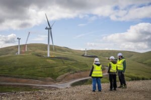 Three people stand in hi-vis jackets looking at construction site at Whitelaw Brae in Scotland.